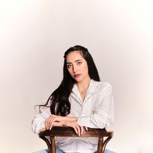 model sat on a wooden chair looking at the camera with red lip stick