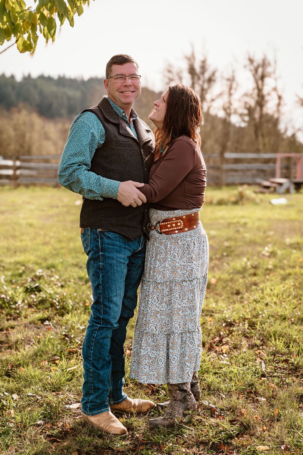 Couple embracing outdoors on a farm in autumn, man in teal shirt and vest, woman in brown top and floral skirt.