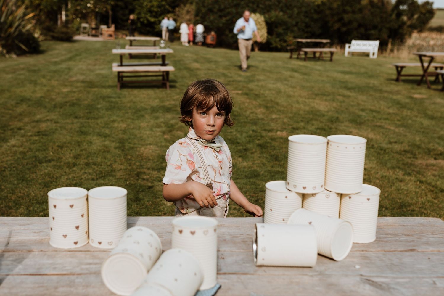 A child in sunglasses sits outdoors next to a stack of white toilet paper rolls on a wooden surface.