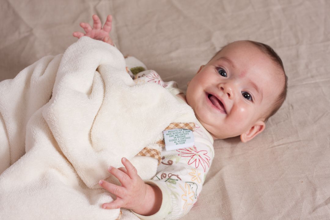 Baby boy with great big smile lying on sheet while wrapped up in baby blanket.