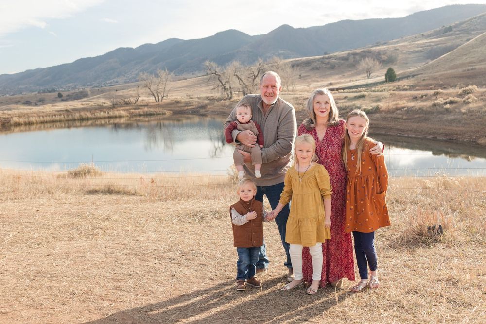 Group portrait in coordinated outfits standing in front of mountainous landscape during golden hour.