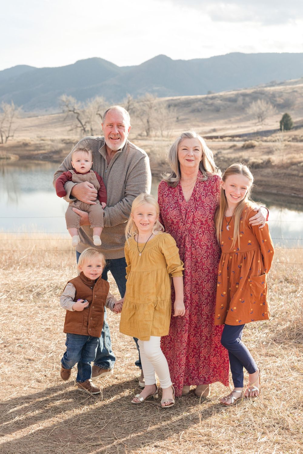 A family poses together in outdoor portraits wearing coordinated fall colors against a mountain landscape.