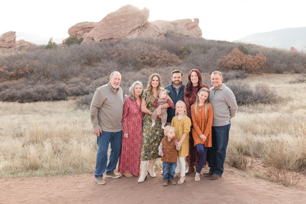 A group poses together on a trail with red rock formations and mountains visible in the background.