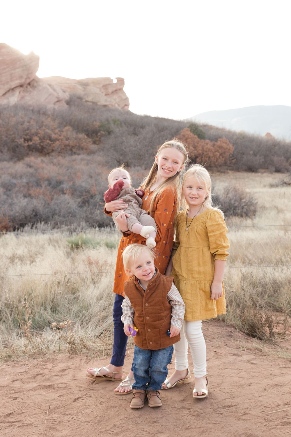 Family members share laughter while posing on a dirt path with desert mountains behind them.