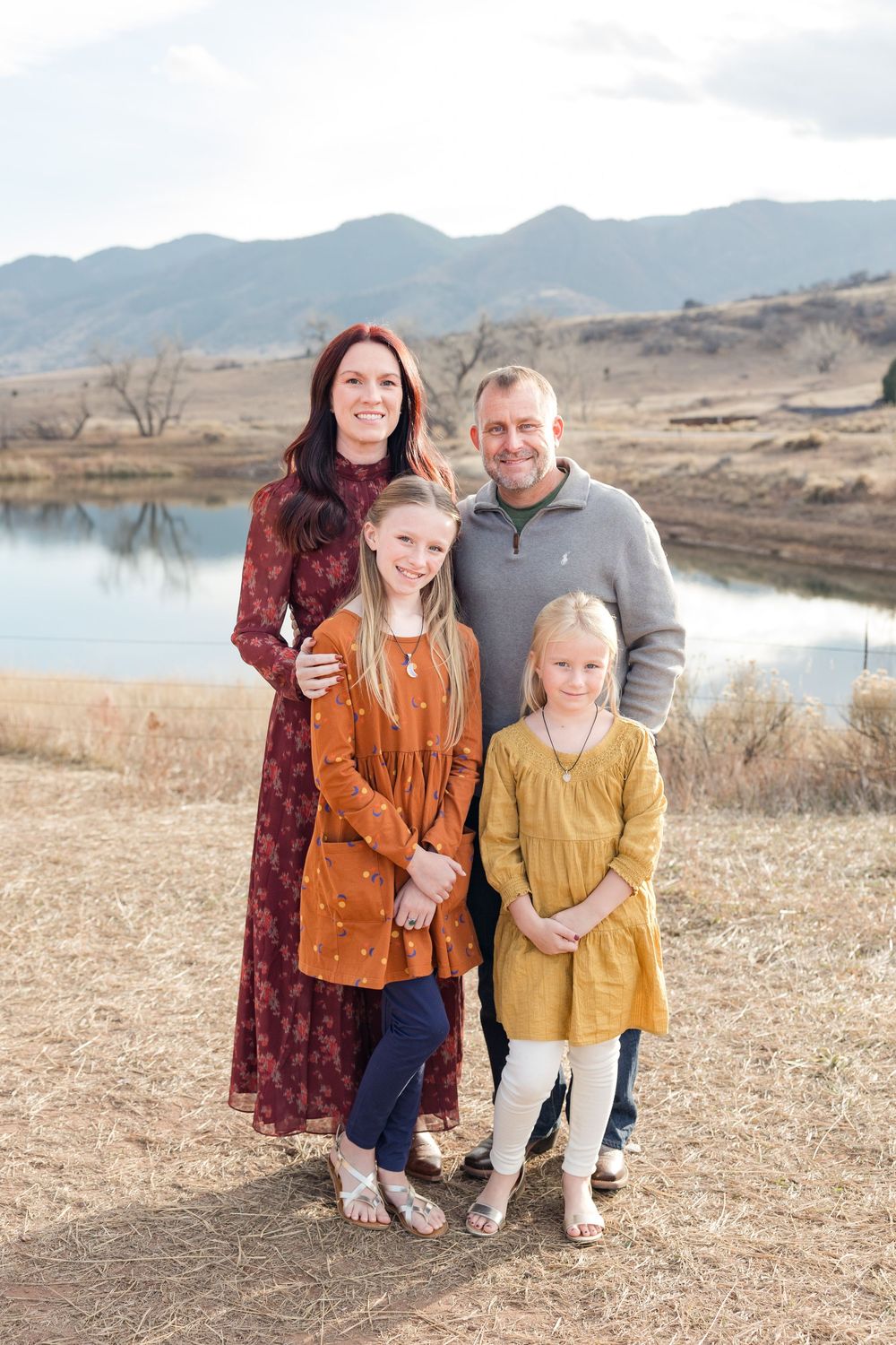 A family poses together in casual attire against a mountain landscape with a lake in the background.