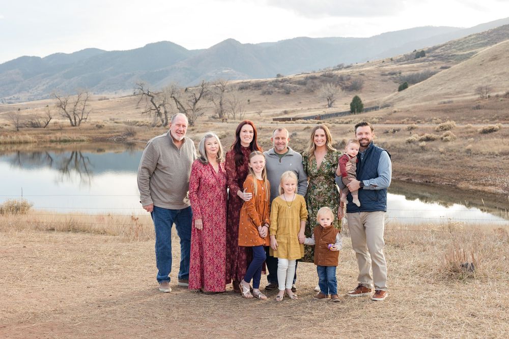 A family group poses together against a scenic mountain landscape backdrop during golden hour.