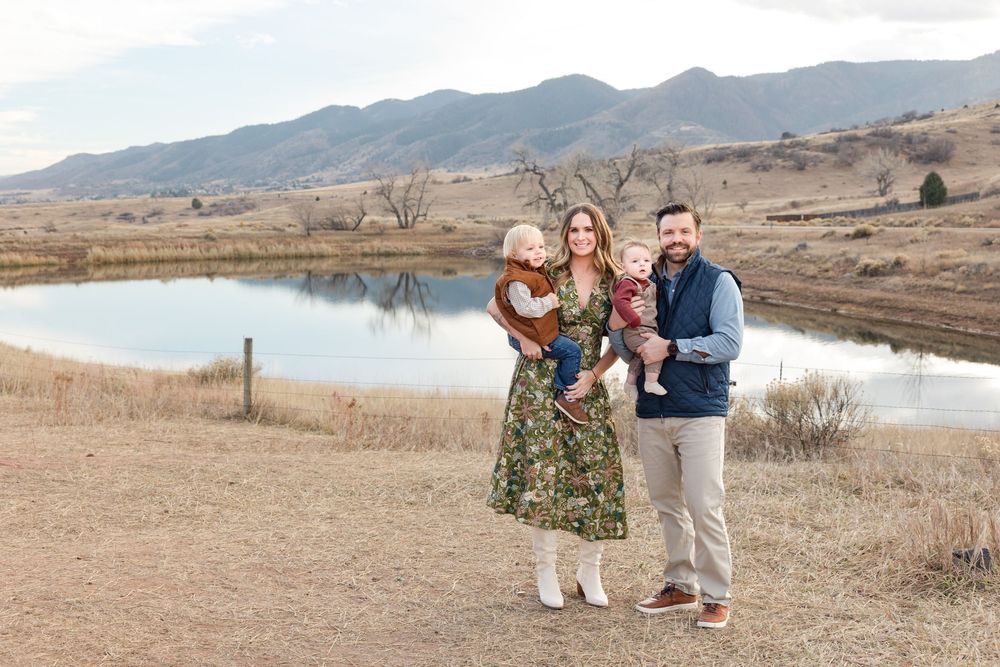 Family portrait session in golden field with mountains and lake in background at sunset.
