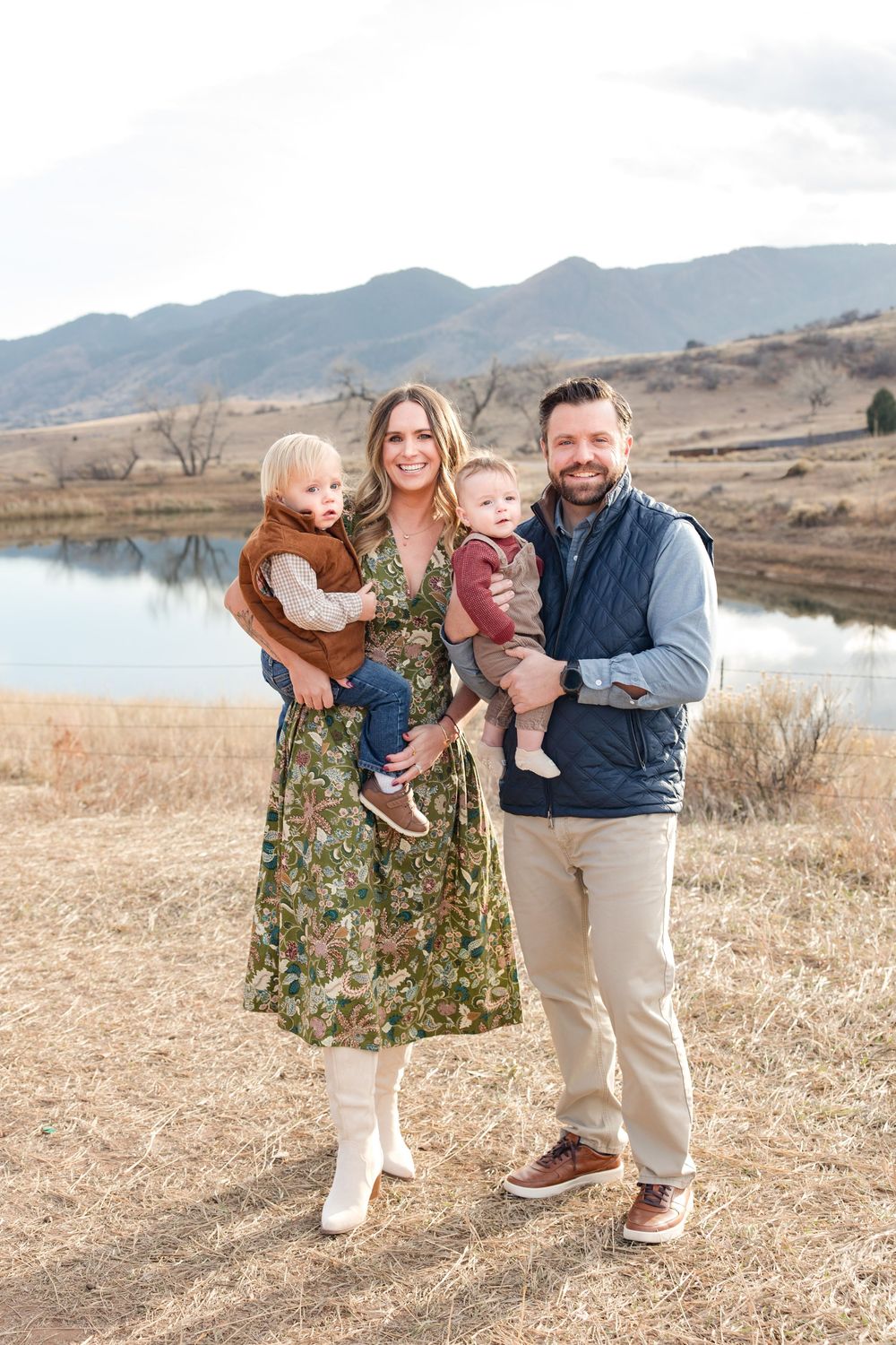 Family members share a playful moment outdoors with mountains and a lake in the distance.
