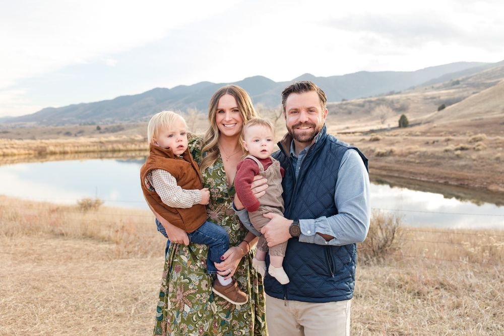 A family poses together in front of a scenic mountain lake landscape on a golden autumn afternoon.
