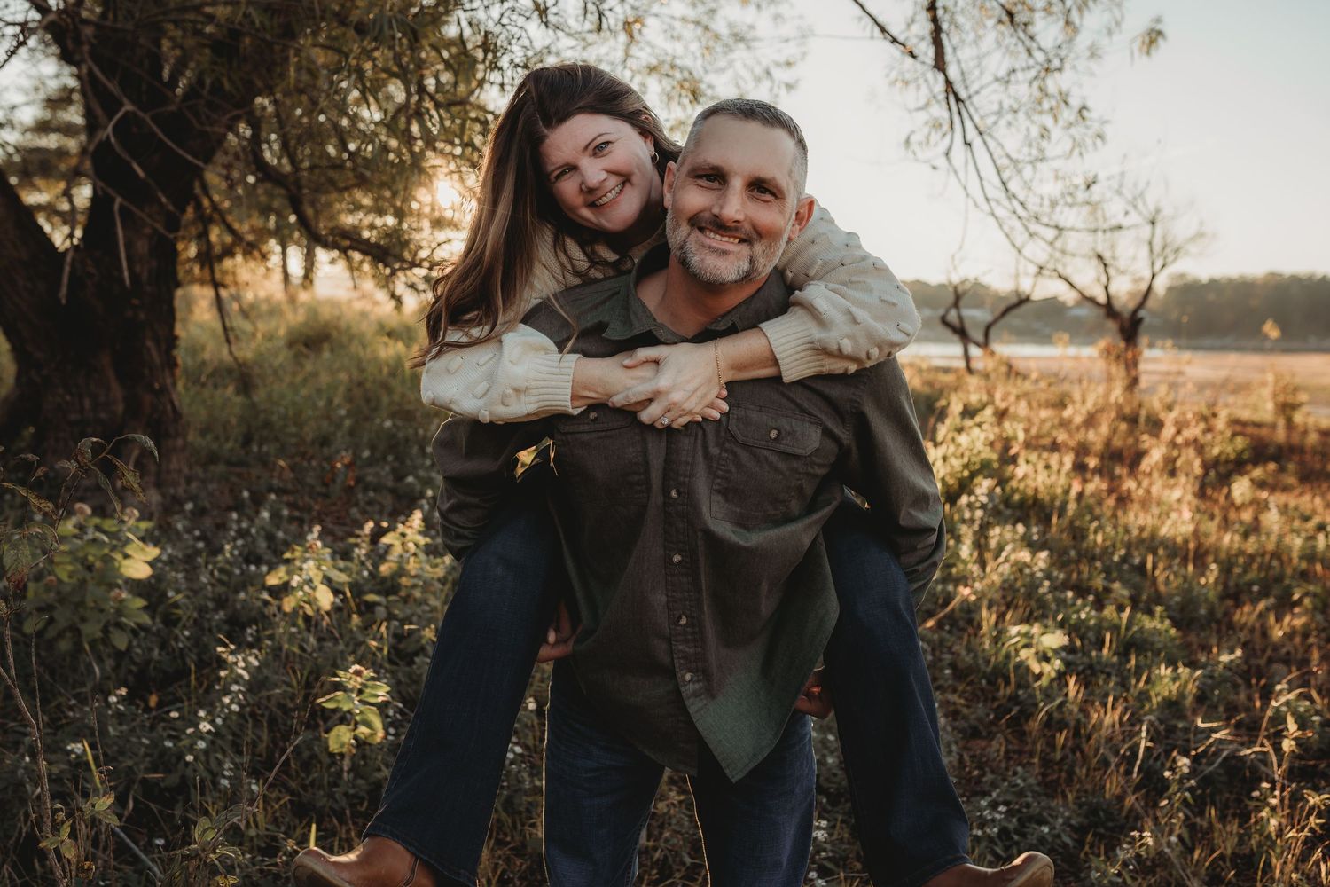 A couple embraces outdoors during golden hour in a natural setting with autumn foliage and warm sunlight.