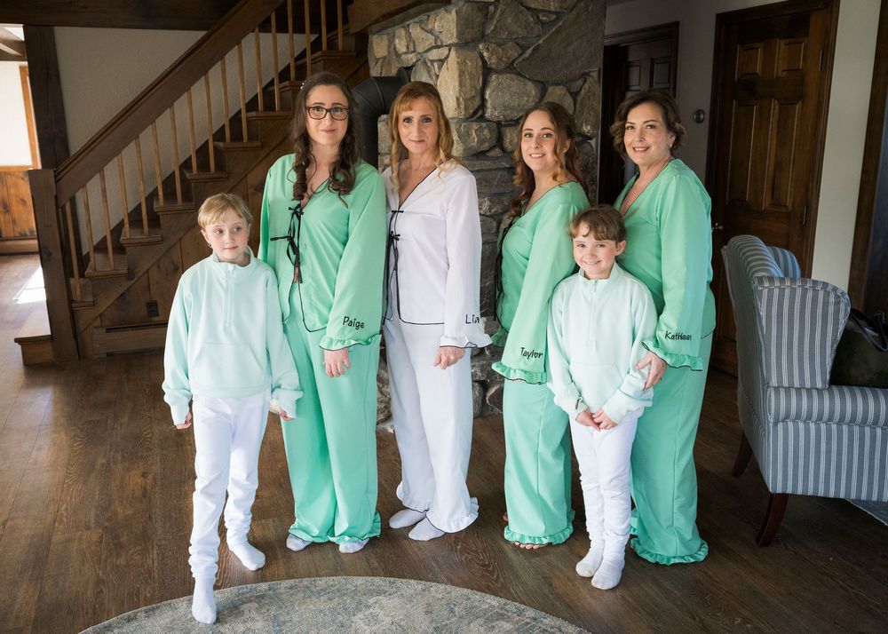 Group of women and two children in matching mint green pajamas posing together indoors near a staircase.