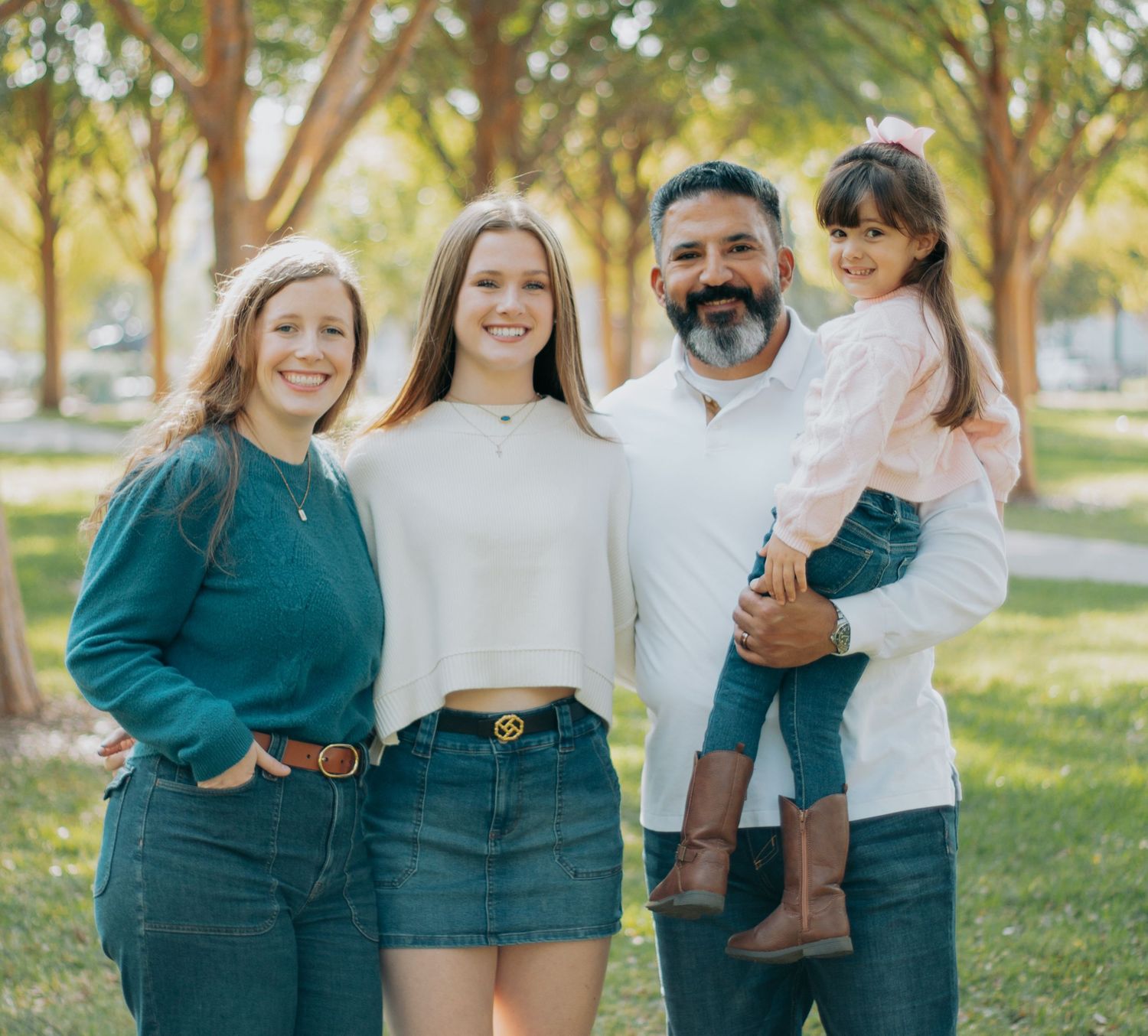 A group of friends in coordinated outfits pose together outdoors in a park during golden hour lighting.