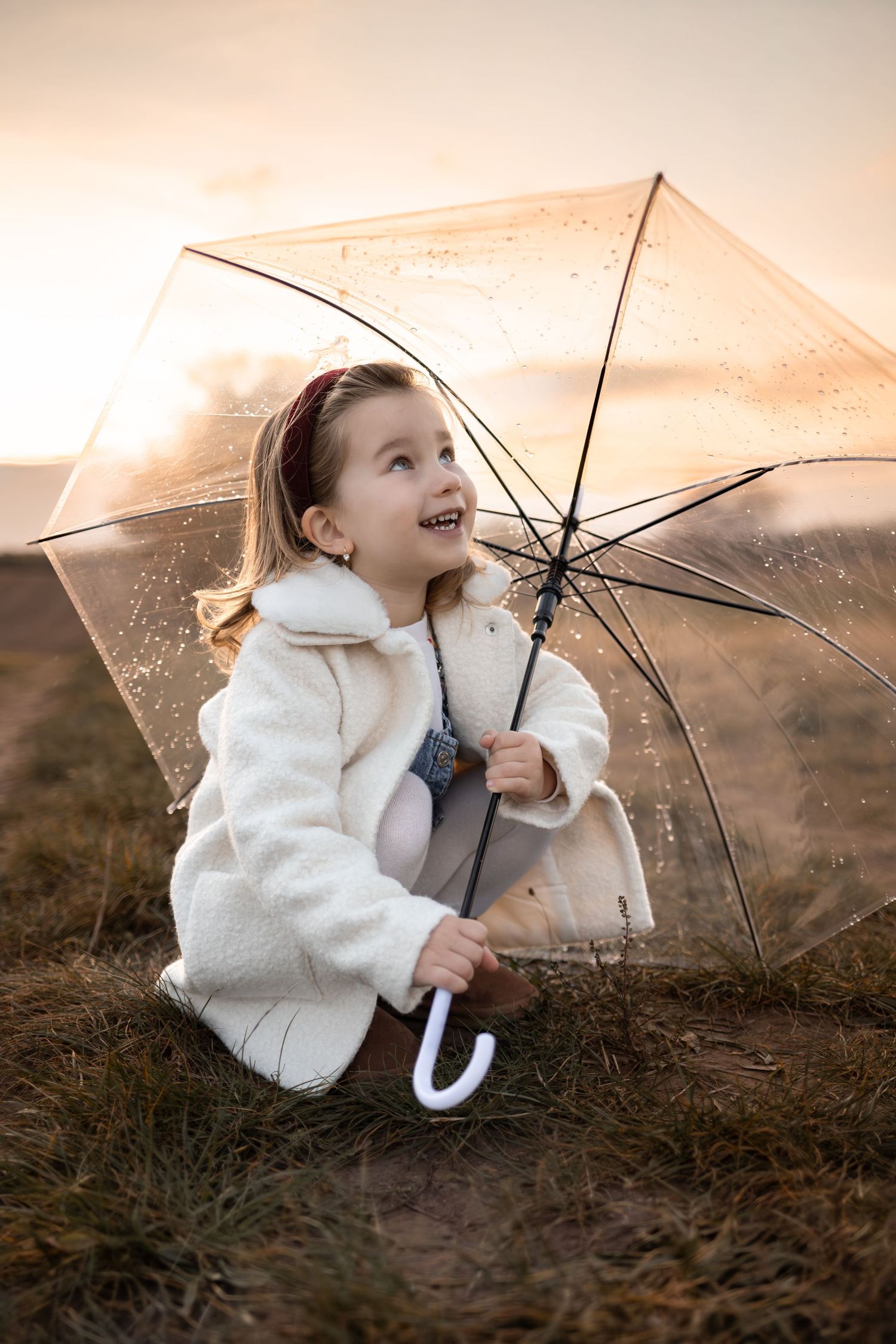 Child playing with clear umbrella during golden hour outdoors.