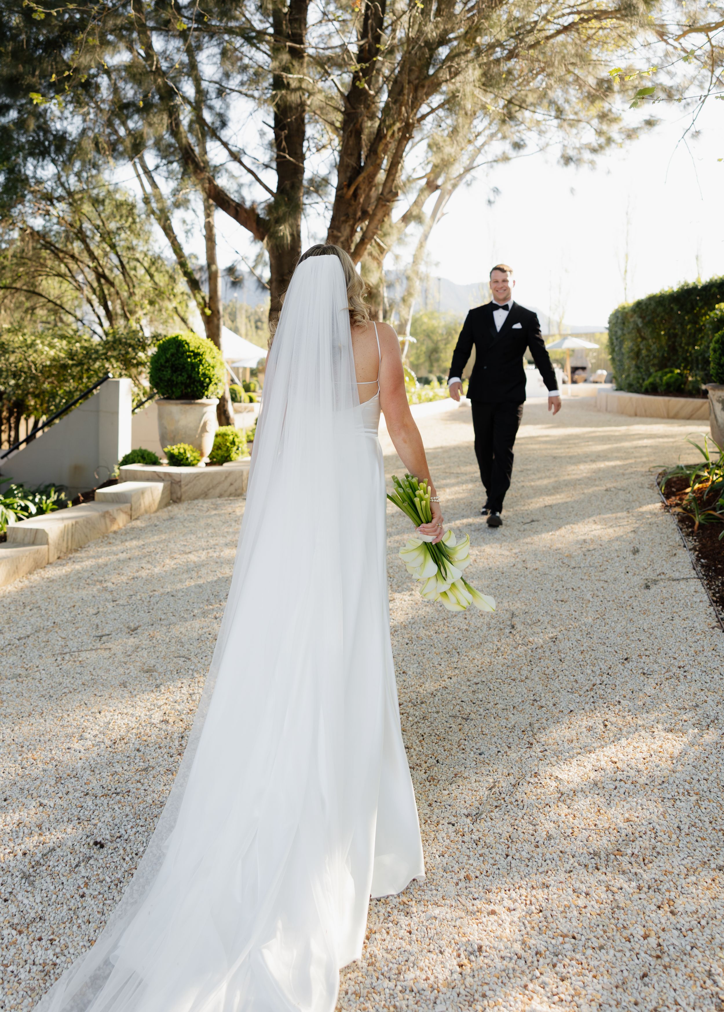 A series of wedding photos showing a couple walking on a gravel path lined with trees in an outdoor garden setting.