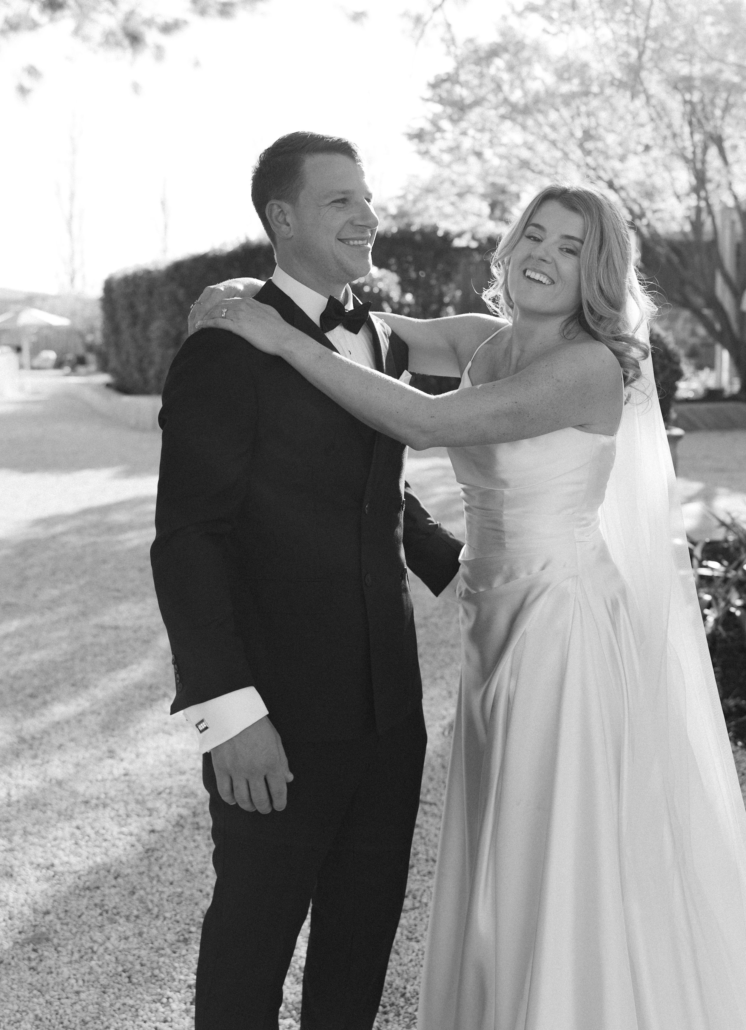 A joyful couple shares a candid moment together outdoors in black and white wedding attire.