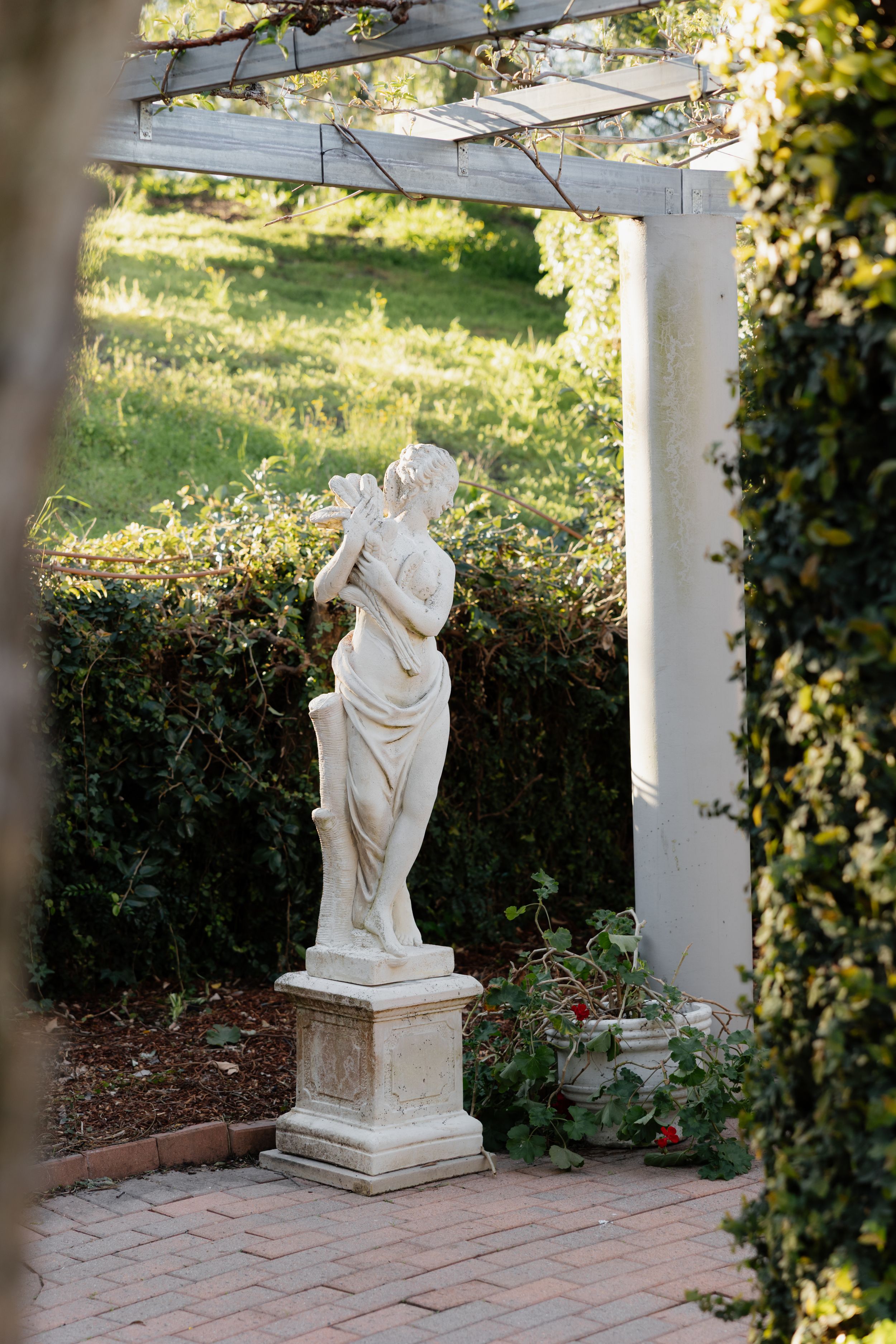 White marble statue in a garden setting with columns and hedges under natural sunlight.