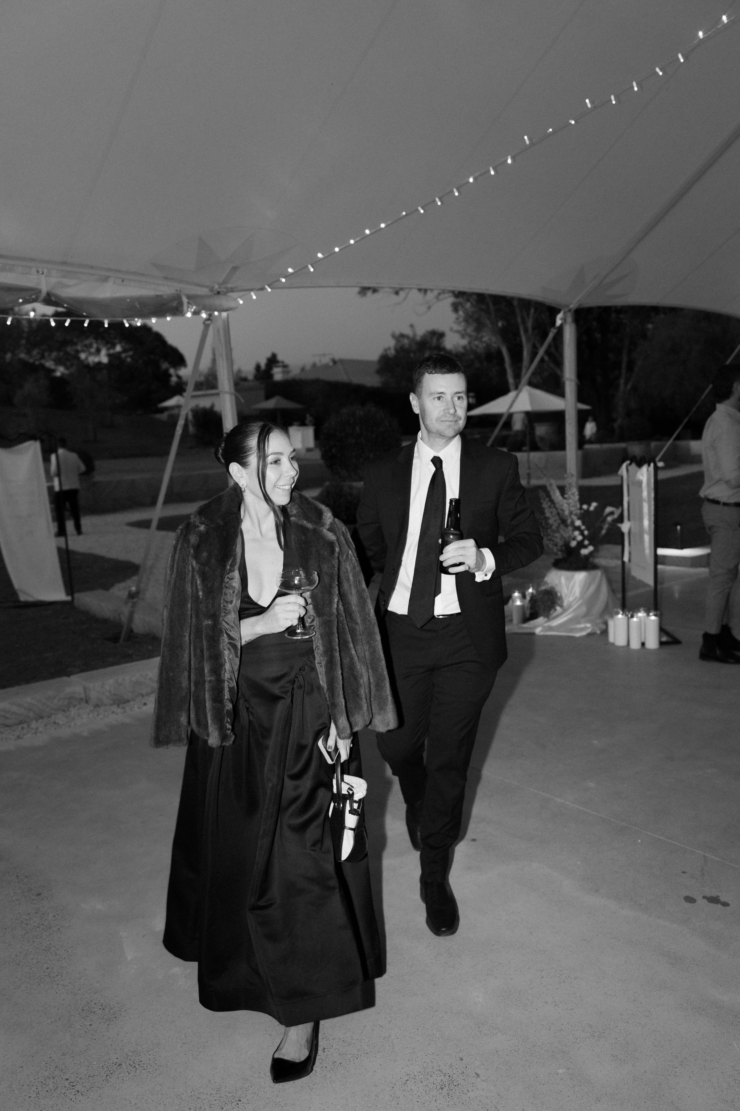 A black and white photo series shows two people walking together under string lights at an outdoor event.