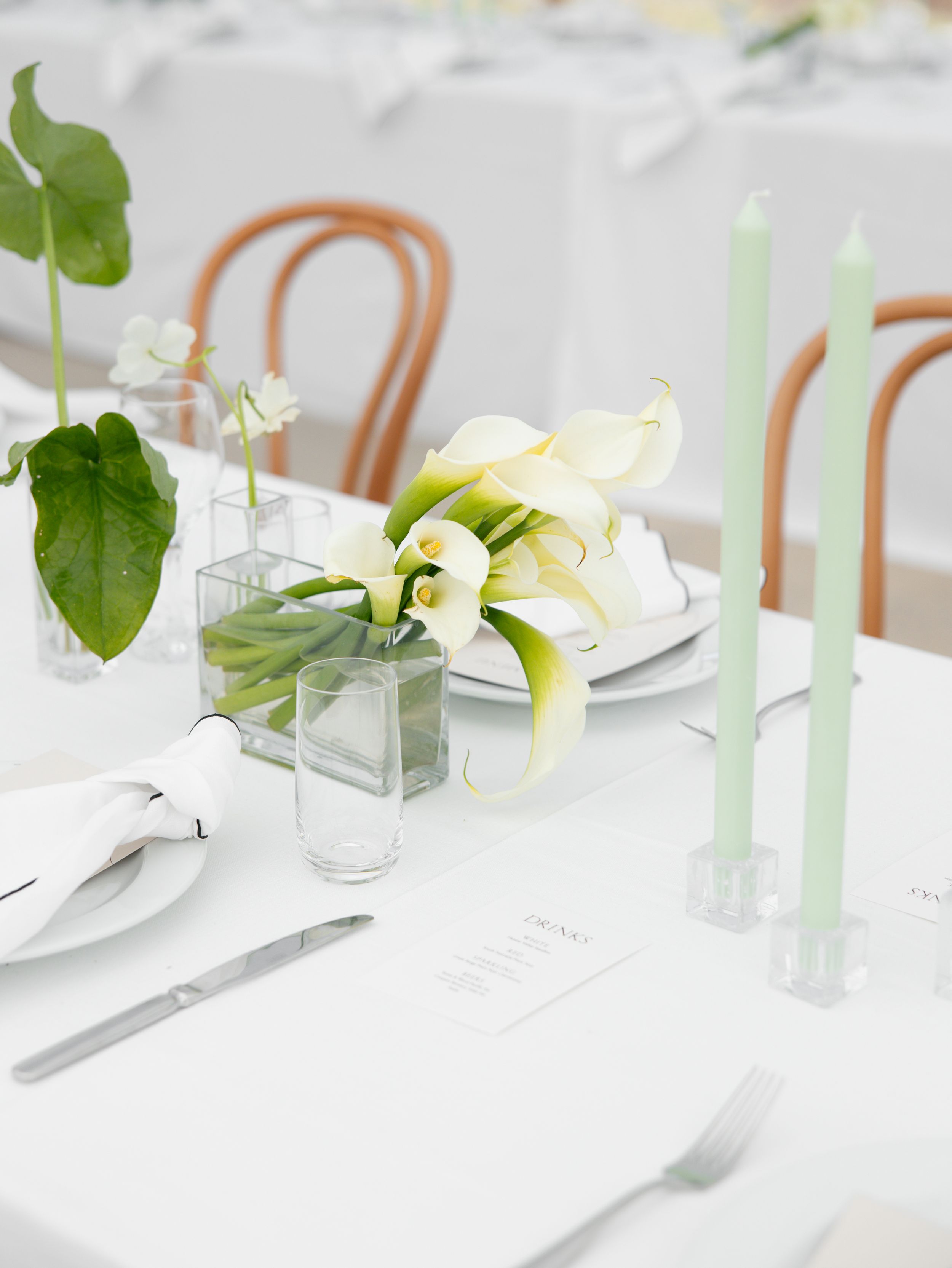 Elegant white table setting with pale green taper candles and delicate floral arrangements in glass vases.