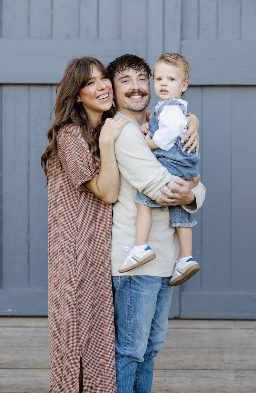 A smiling family poses in front of a pale blue wooden farmhouse door at Saltonstall Farm in Stratham, New Hampshire for family photos.