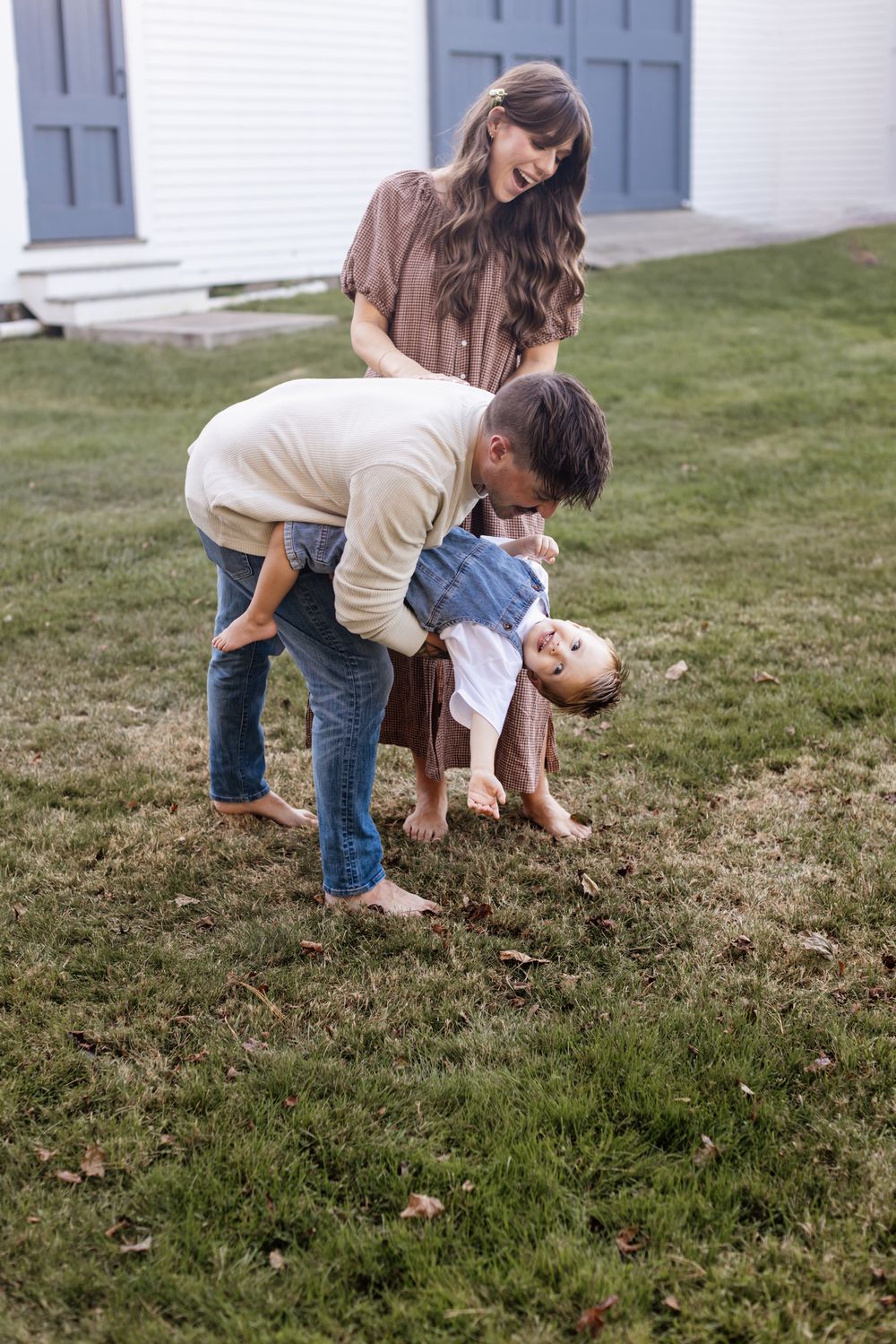 Father bends his son low playing with him while a smiling mother in a gingham dress looks on at Saltonstall Farm in Stratham, New Hampshire