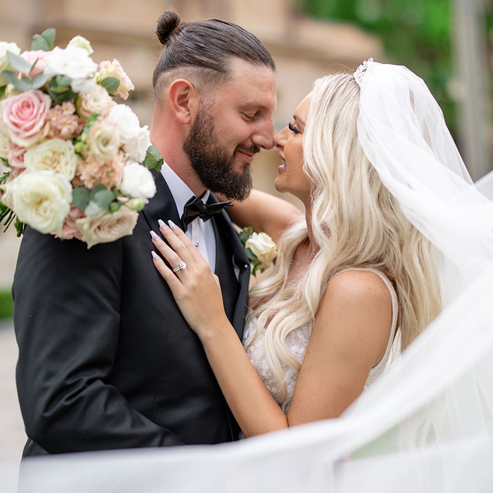 Romantic moment between newlyweds as groom in tuxedo and blonde bride in veil share a tender kiss.