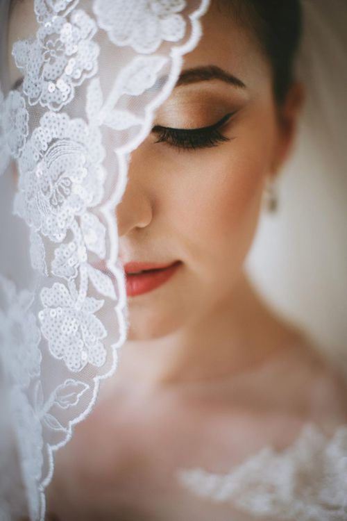 Close-up portrait of a bride with flawless makeup, eyes closed, framed by a delicate lace veil.