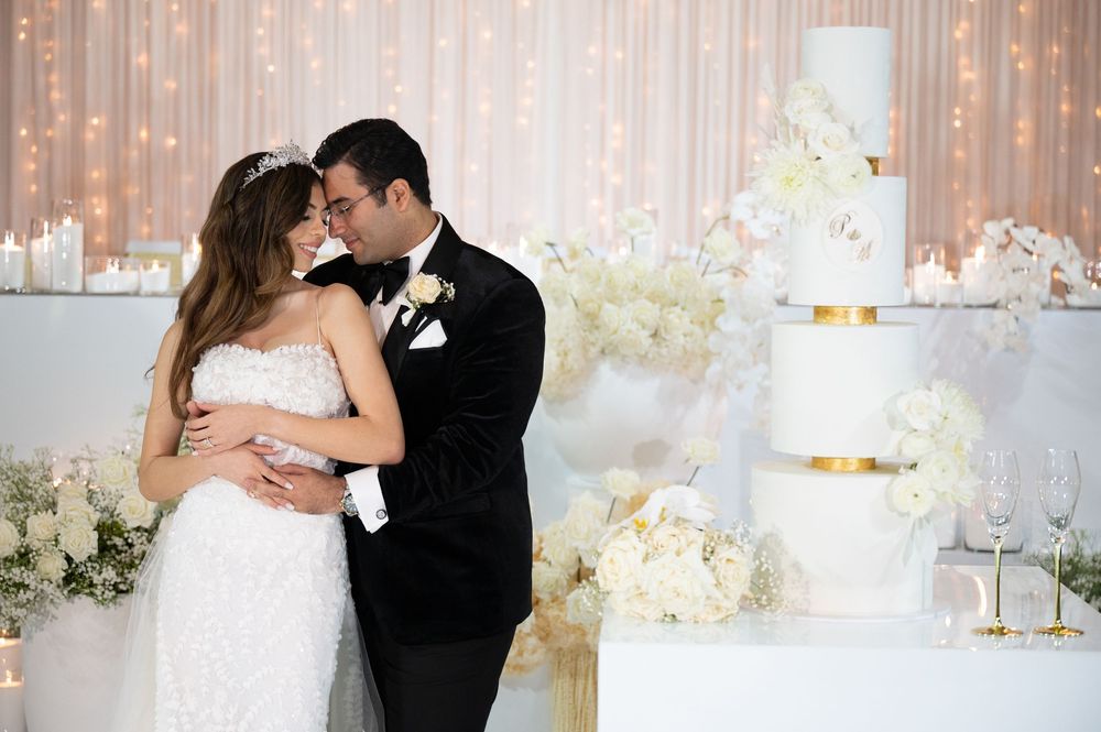 Bride and groom sharing romantic moment beside elegant white and gold tiered wedding cake.