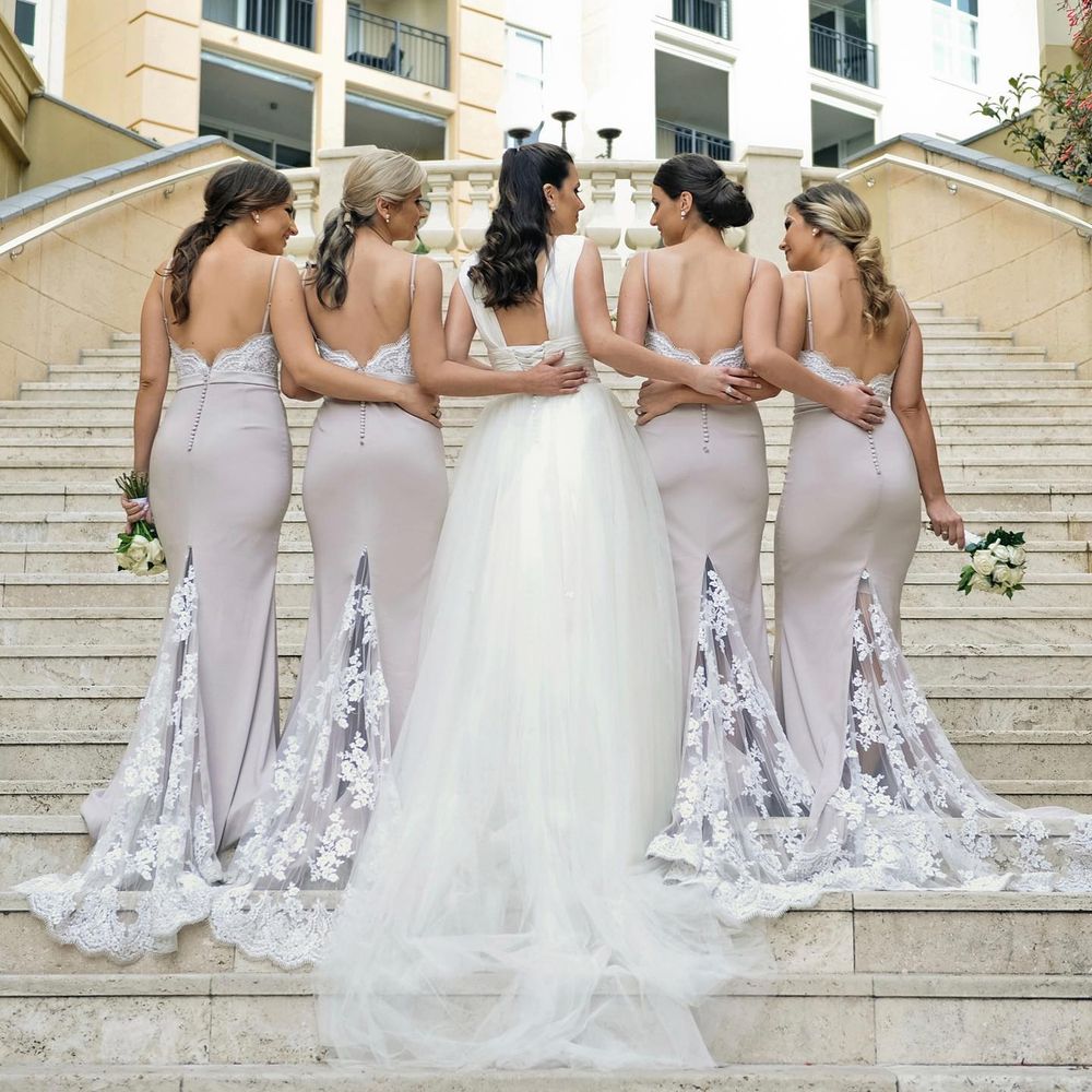 Bride with four bridesmaids in backless gray gowns pose on outdoor staircase showing elegant lace train details.