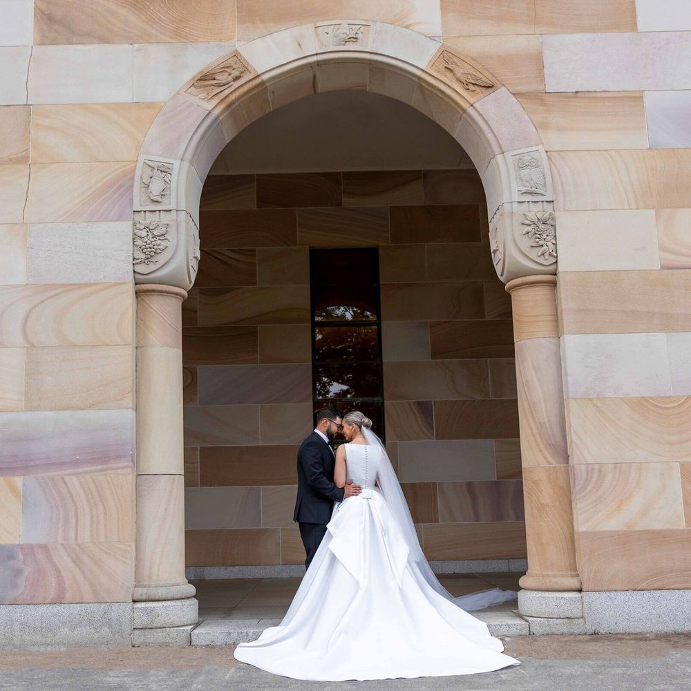 Bride and groom share a tender kiss under an ornate sandstone arch at a historic wedding venue.