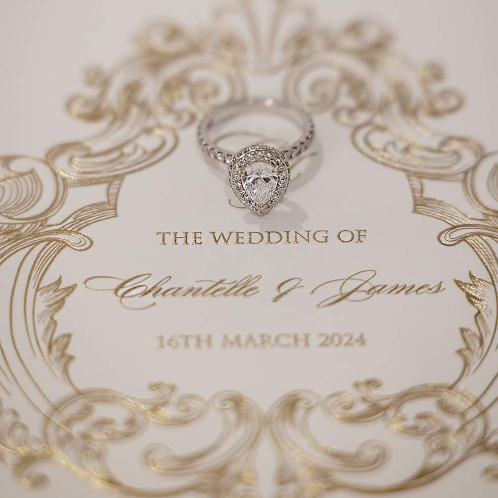 Diamond halo engagement ring rests on elegant wedding invitation for Chantelle and James, 16th March 2024.