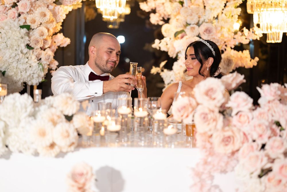 Bride and groom toasting champagne at sweetheart table surrounded by pink roses and candlelight.