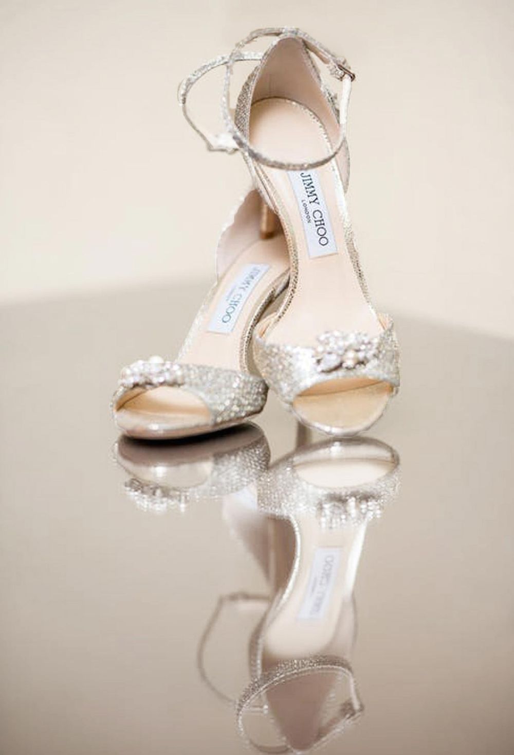 Sparkling Jimmy Choo bridal heels with pearl embellishments reflected on glossy surface.