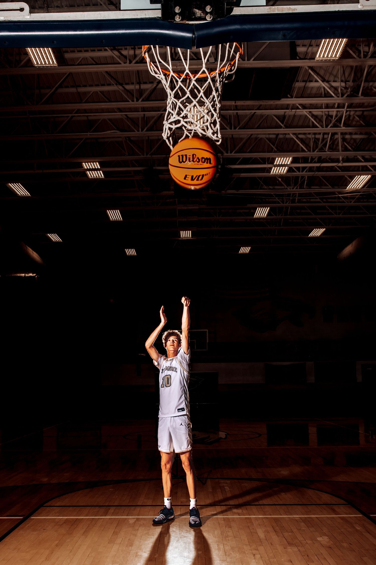 Basketball player in white uniform shooting a free throw on indoor court with Wilson ball going through hoop net.