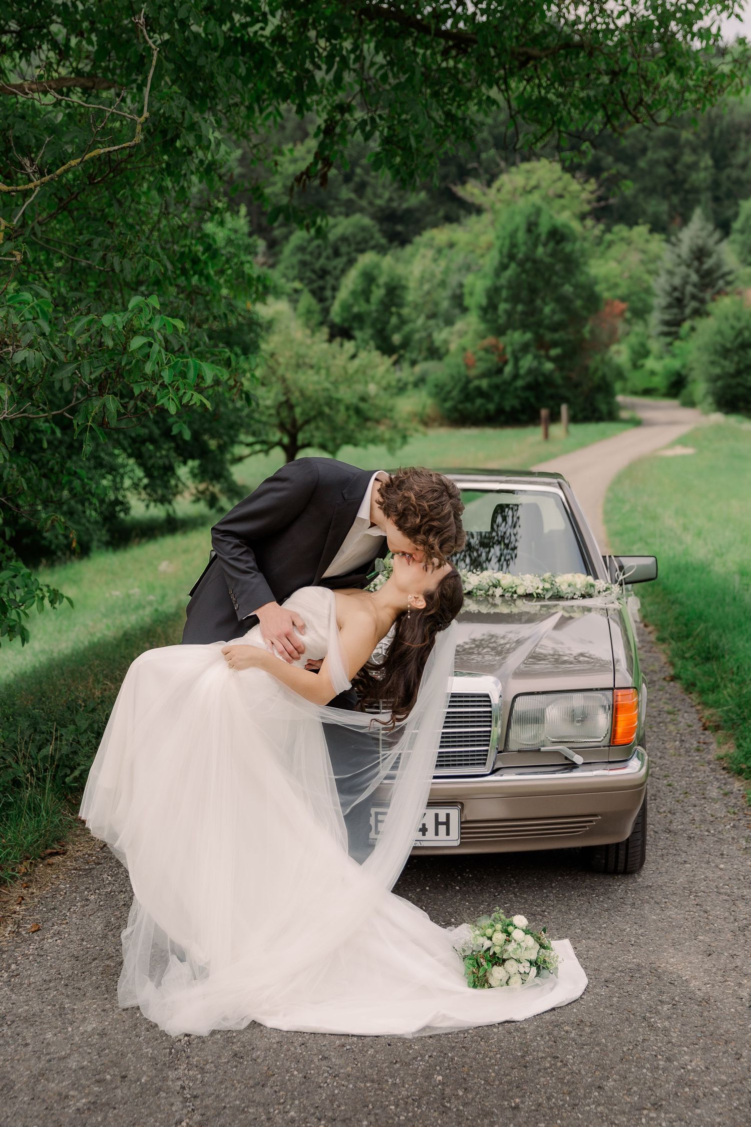 White wedding dress flowing over vintage car during outdoor photo session.