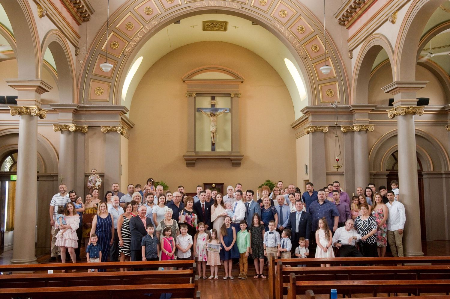 Wedding guests stand together in a traditional church sanctuary with ornate architectural details and vaulted ceilings.