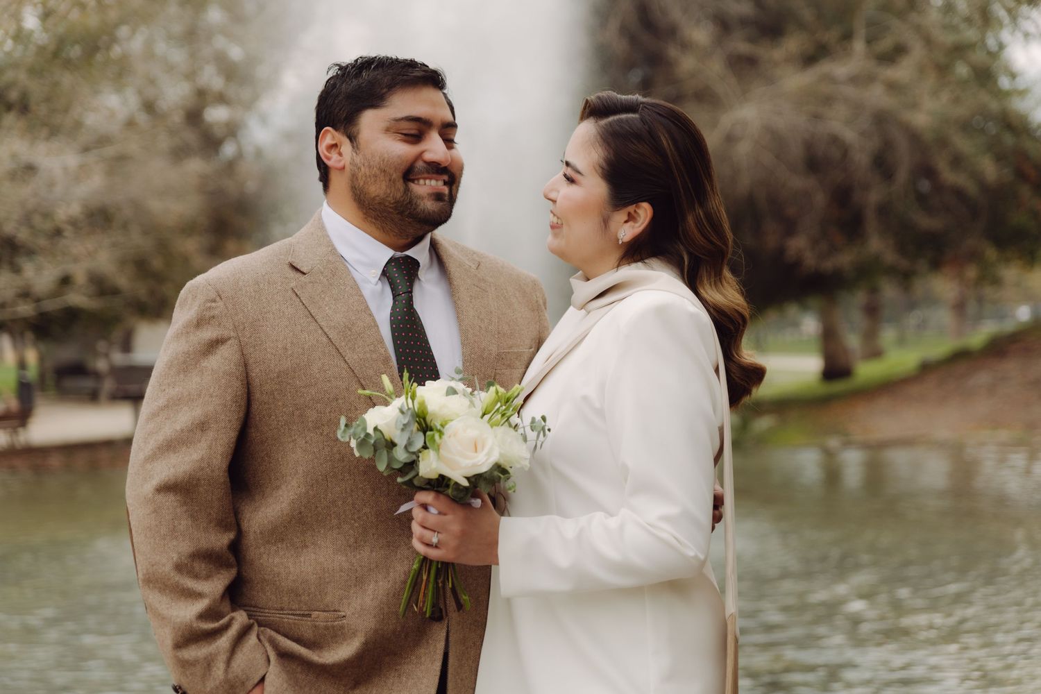 Bride and groom smiling at each other holding a white floral bouquet.