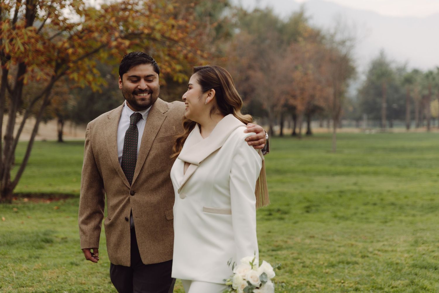 Happy newlywed couple sharing a joyful moment while walking together in an autumn park.