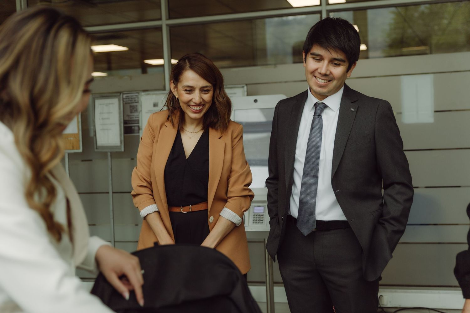 Business professionals smiling and chatting in modern office corridor during casual meeting.