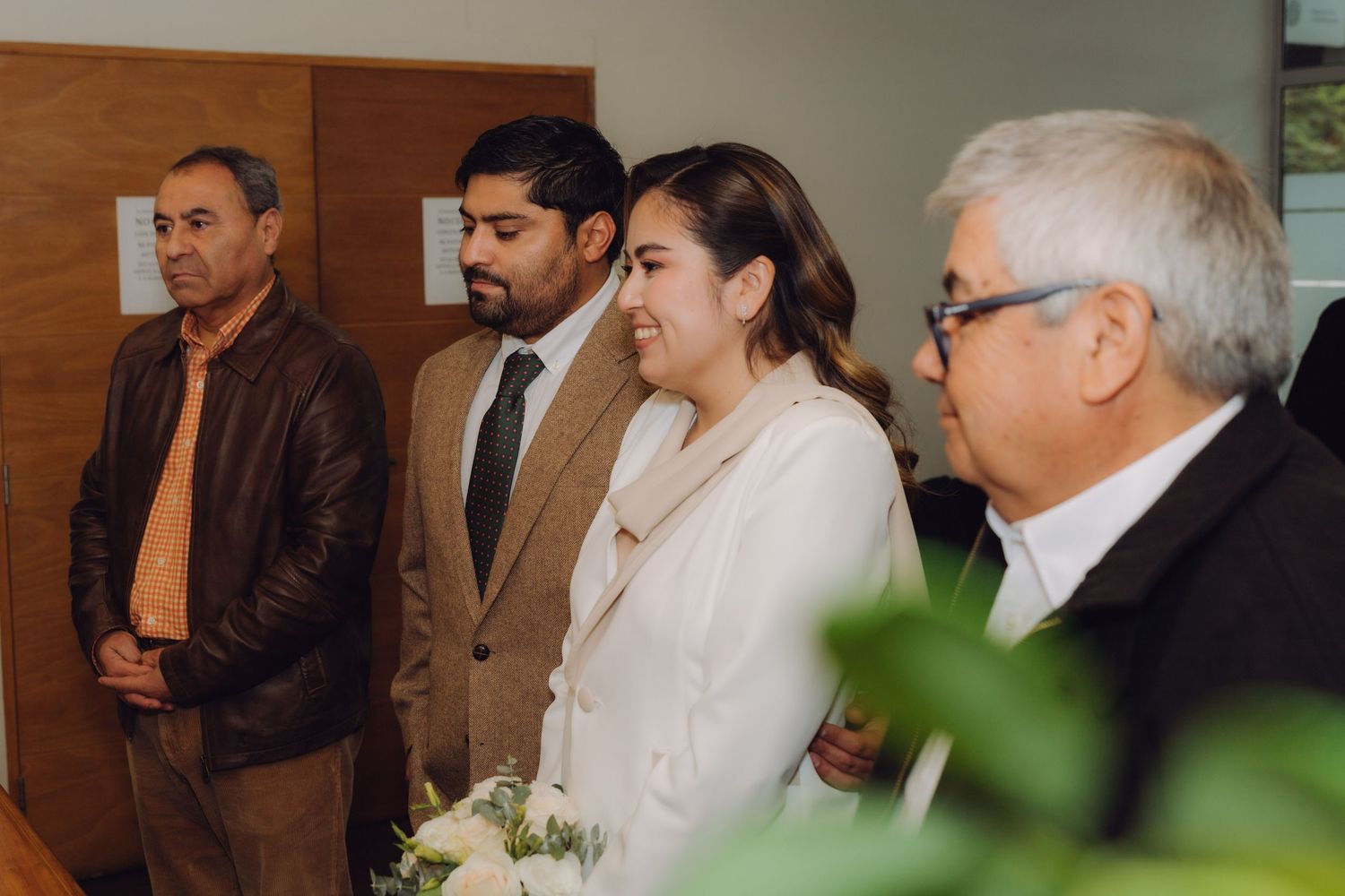 Bride holding white bouquet standing with groom and family during civil wedding ceremony.