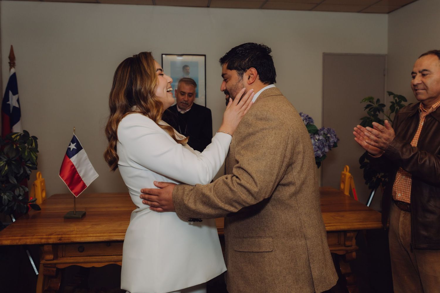 Newlyweds embracing after civil wedding ceremony with Chilean flag and guests applauding.