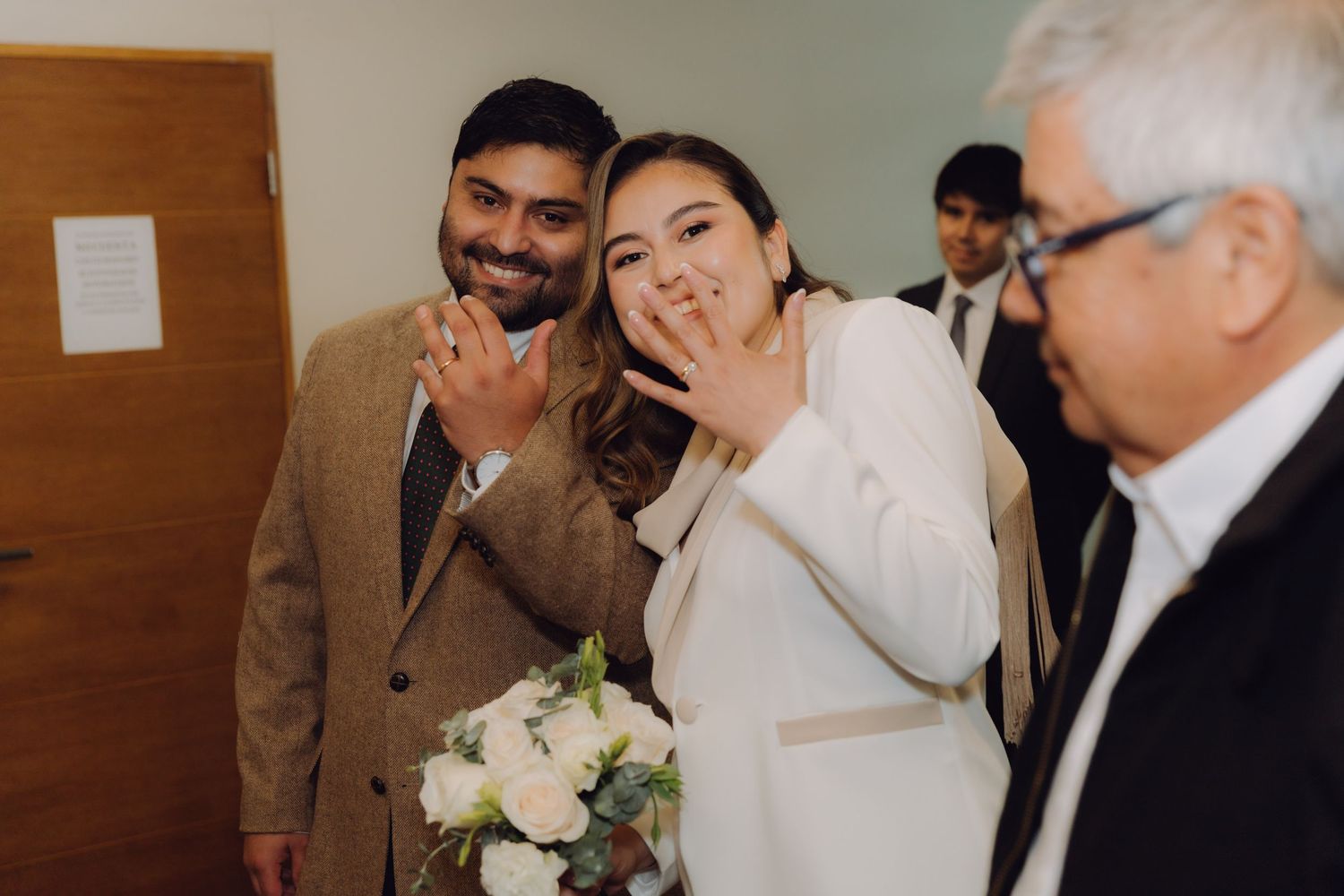 Happy newlyweds displaying wedding rings to camera while holding white floral bouquet after civil ceremony.