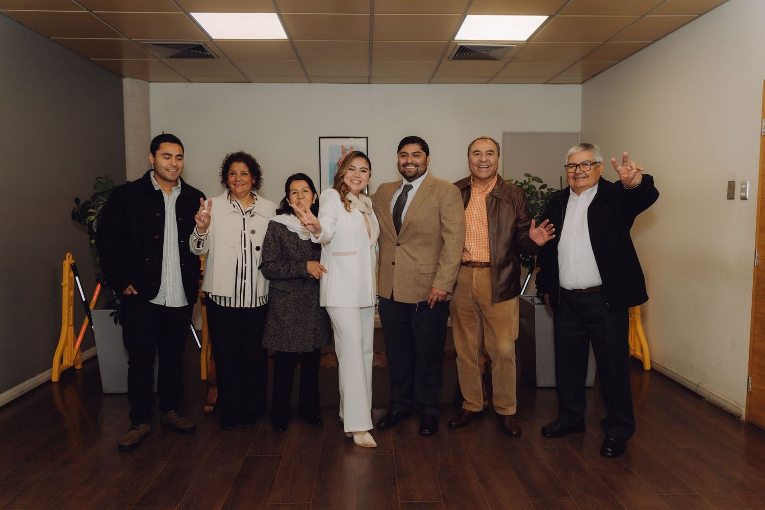 Group of seven wedding guests celebrating and posing together in formal office setting.