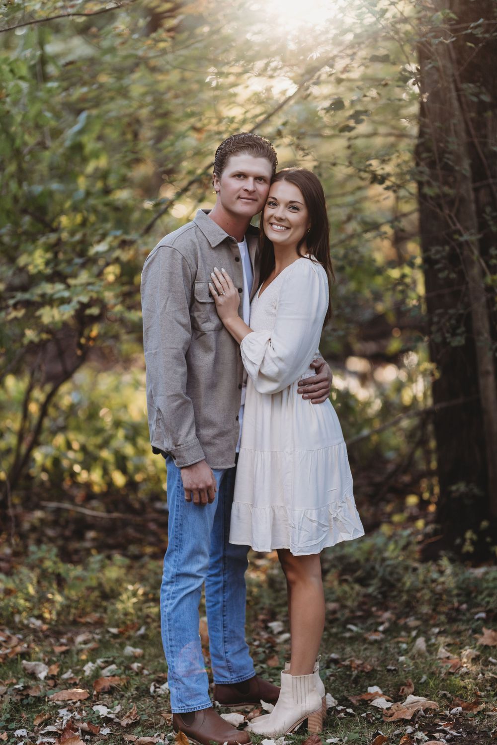 A couple shares a romantic moment in a wooded outdoor setting during an autumn engagement photoshoot.