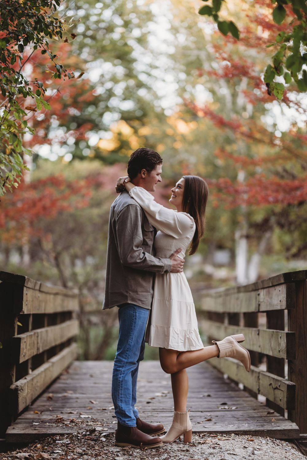 A romantic moment shared on a wooden bridge surrounded by vibrant fall colors.
