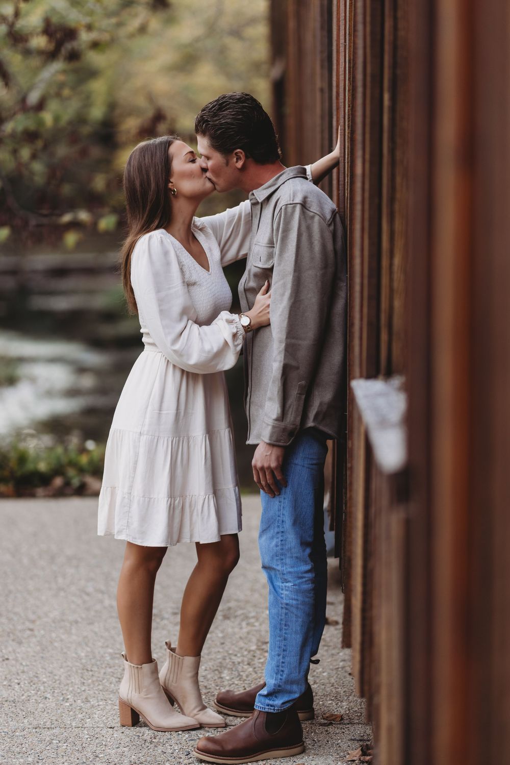 A couple shares intimate moments against a rustic brown wall outdoors.