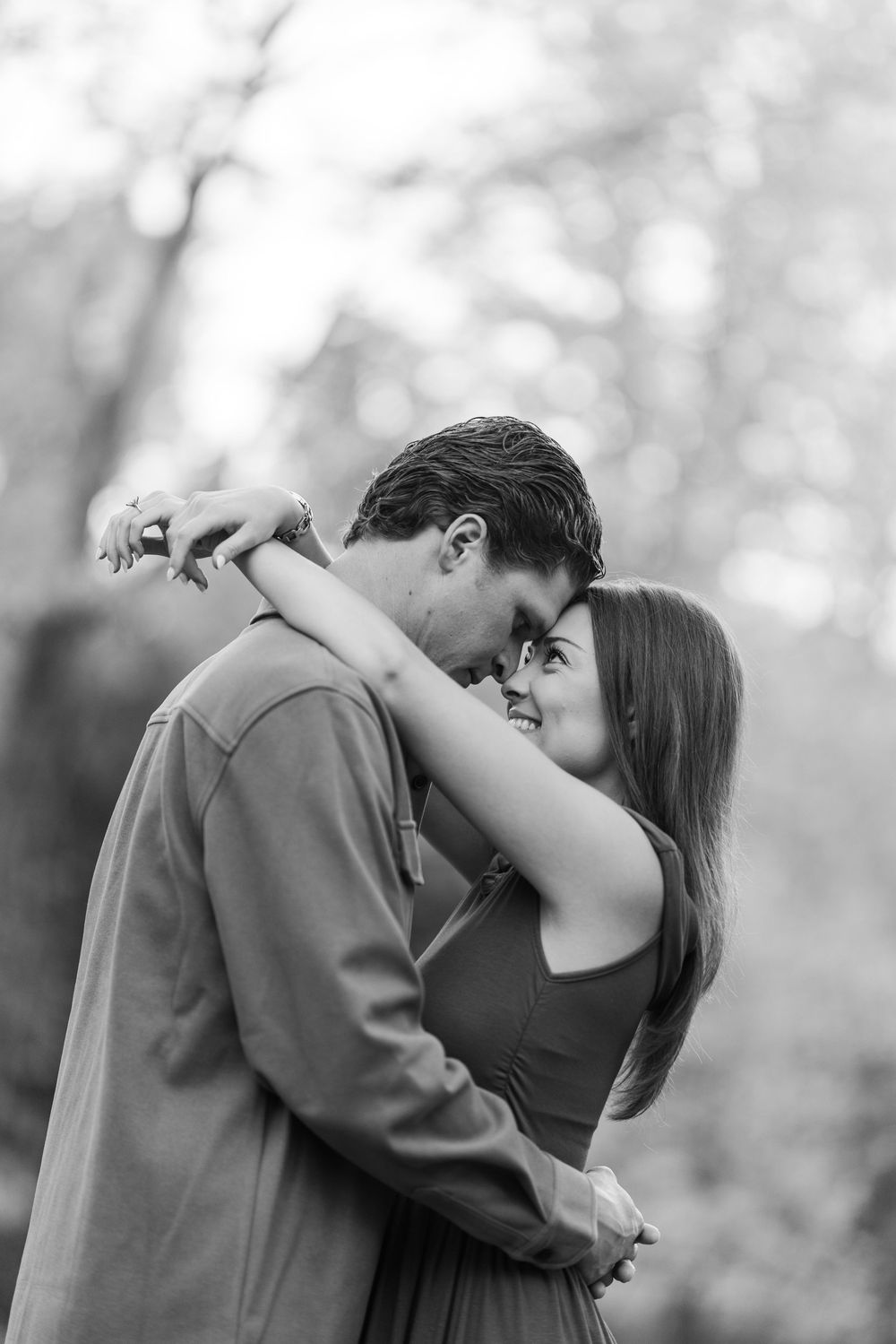 A romantic couple shares an intimate embrace and kiss in a dreamy black and white outdoor setting.