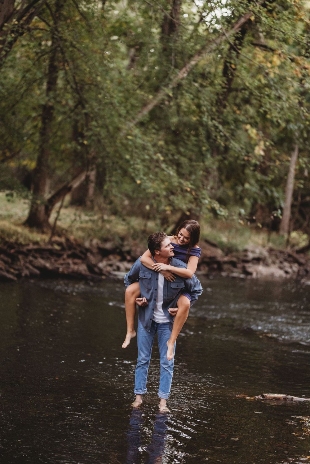 Playful couple sharing a piggyback ride while standing in a forest stream.