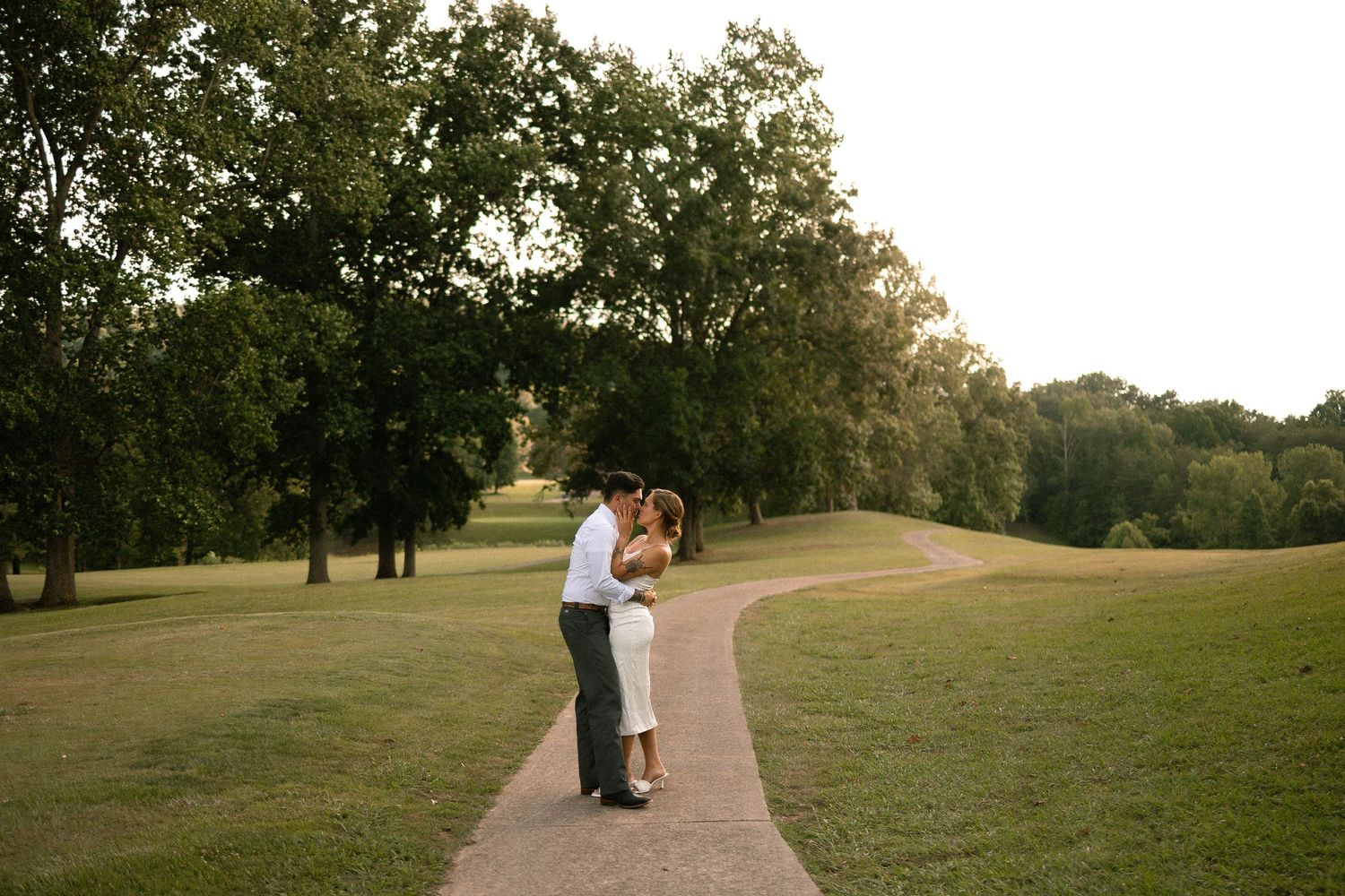 A couple embraces on a winding path through a scenic golf course at sunset.