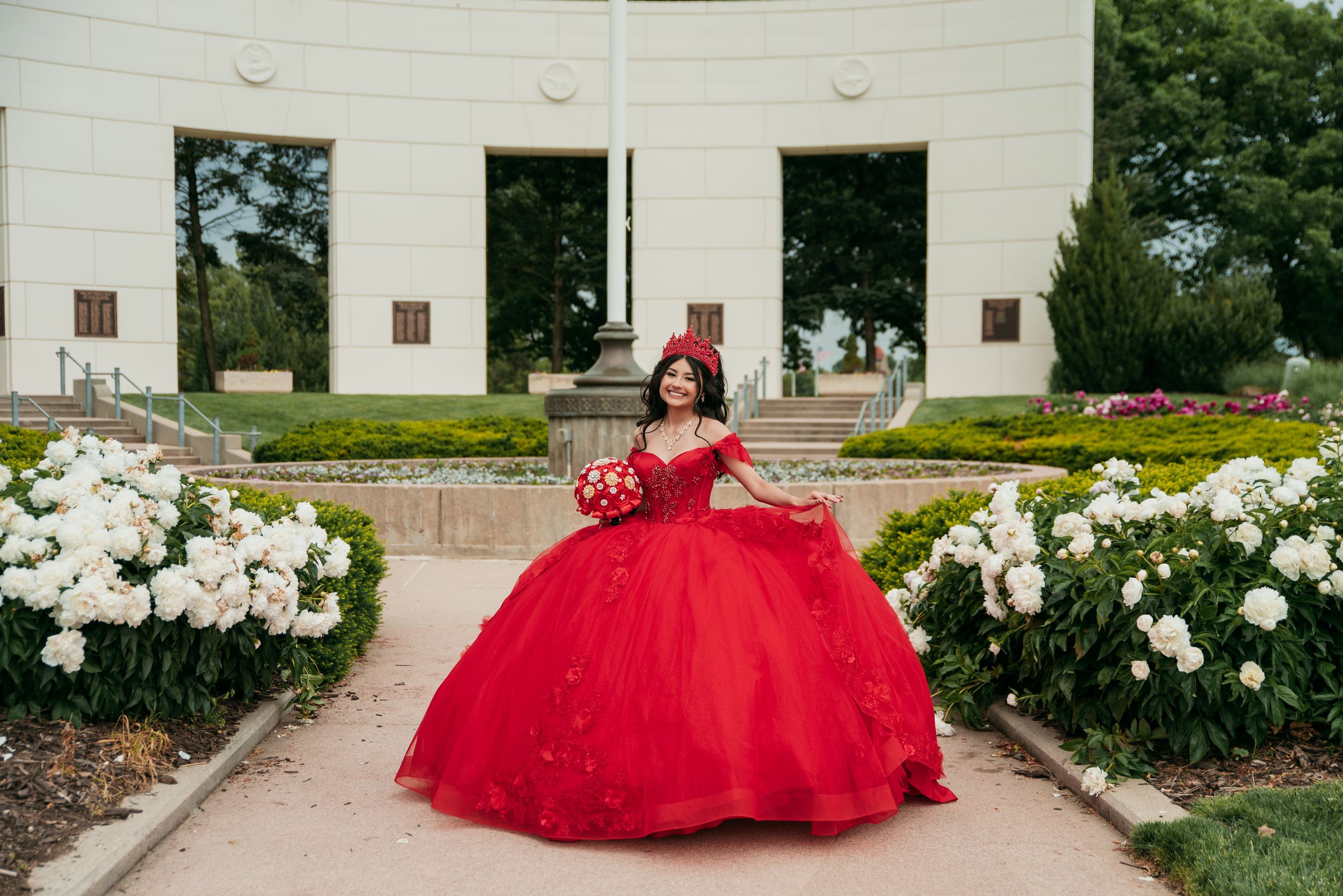 Elegant quinceañera photos featuring red ballgown against white architectural backdrop with gardens.