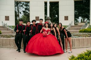 Quinceañera celebration with court members in formal attire posing on outdoor stone steps.
